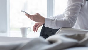 hand holding cell phone with white coffee cup and neutral background