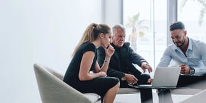 woman and two men looking at laptop around table